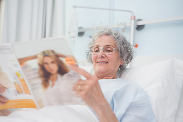 Obraz premium Elderly patient reading a magazine on her bed