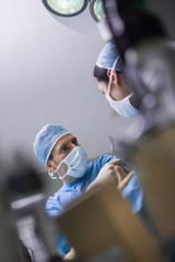 Serious doctor giving a surgical scissor to a nurse