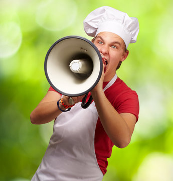 portrait of young cook man screaming with megaphone against a na