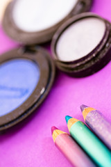 blue eyepencils and eyeshadows on purple background