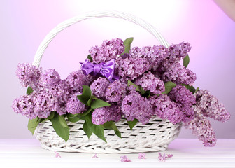 beautiful lilac flowers in basket on purple background
