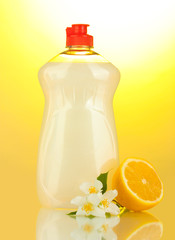 Dishwashing liquid, lemon and flowers on yellow background