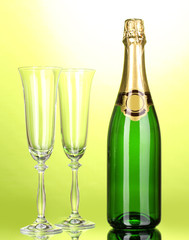 Bottle of champagne and goblets on green background