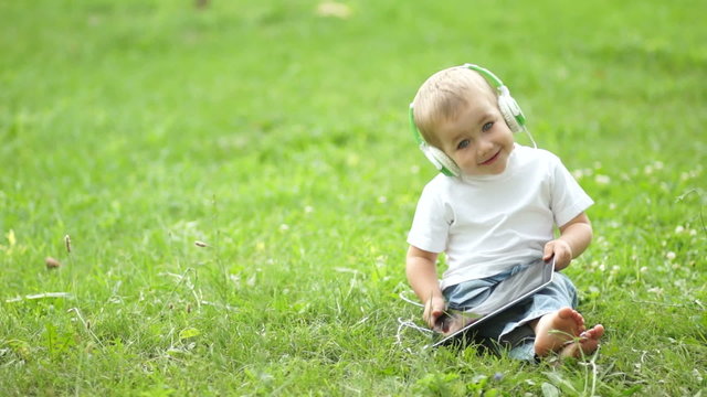 Happy child with a tablet PC sitting on the grass
