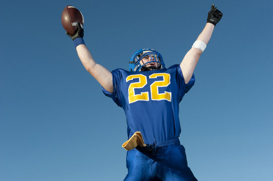 Caucasian football player holding football with arms raised