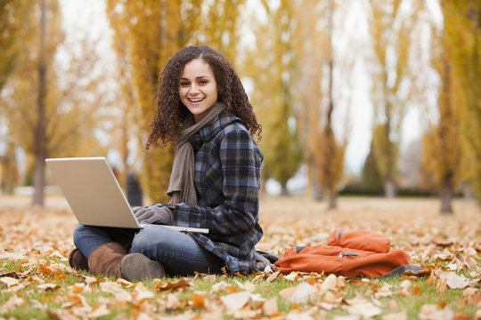 Caucasian woman using laptop in autumn leaves