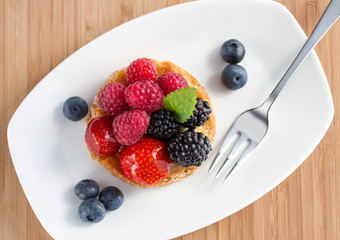 fruit cake with berries on white plate with a fork, top view