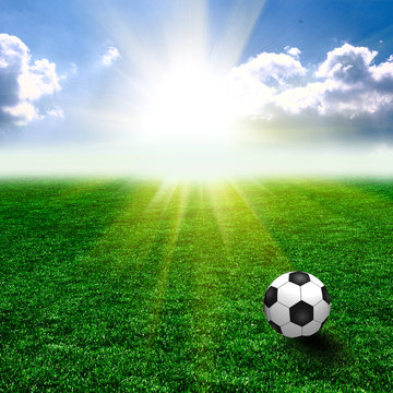 A fine green meadow with a soccer ball on it. All on sky sunset