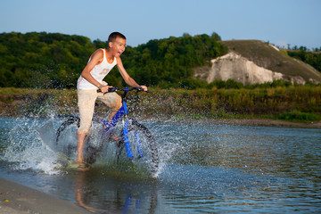 A boy rides his bike along the river
