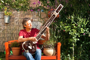 Älterer Mann sitzt in seinem Garten und spielt Sitar
