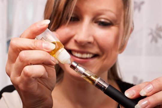 junge blonde Frau bef&uuml;llt mit Liquid ihre elektrische Zigarette
