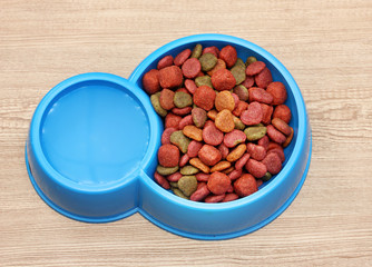 dry dog food and water in blue bowl on wooden background