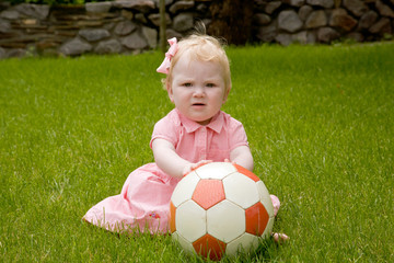 Baby girl sitting on lawn with the ball.