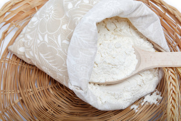 Flour and wheat grain with wooden spoon on a wicker basket.