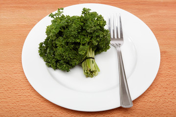 fresh bunch of parsley on the plate with a fork on a wooden tabl