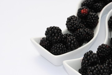 juicy blackberries into shaped dishes, on white background