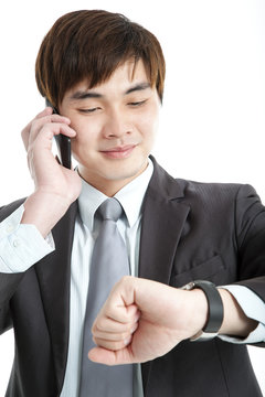 Asian Businessman Checking Time While Talking On Mobile Phone