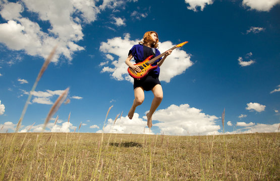 Redhead girl jumping with guitar at outdoor.