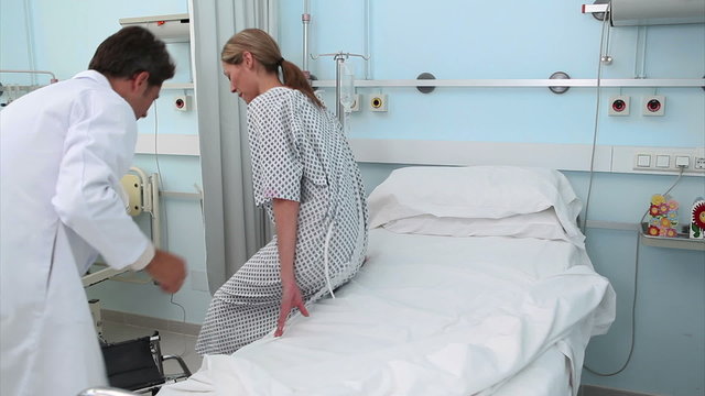 Doctor assisting a patient to lie on a bed
