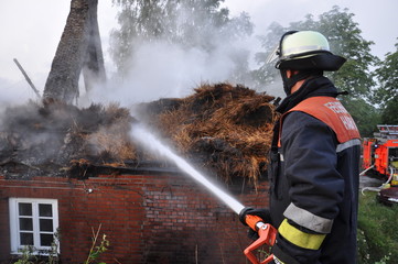 Fototapeta premium Feuerwehrmann löscht Reetdach