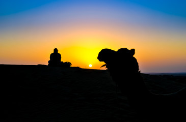 A woman and a camel at sunset on the Thar Desert, India