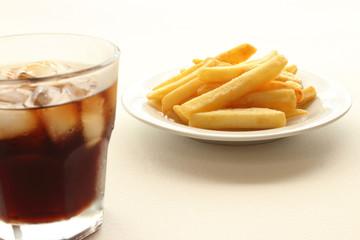 Glass of cola and fried potatoes on plate