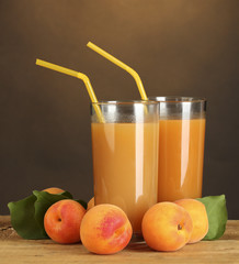 glasses of apricot juice on wooden table on brown background