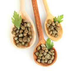 green capers in wooden spoons on white background close-up