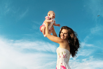 Fototapeta na wymiar Happy mother playing with baby over blue sky