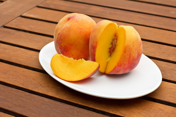 Two fresh peaches on while oval plate on woden background