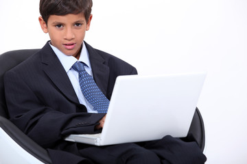 Young boy dressed in an adult business suit with a laptop