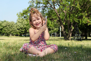 Fototapeta premium little girl sitting on grass and playing with tablet