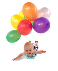 Fototapeta na wymiar bébé souriant allongé sur le sol et ballons colorés