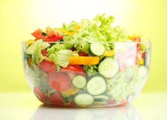 fresh vegetable salad in transparent bowl on green background