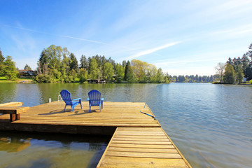 Lake waterfront with pier and two blue chairs. - obrazy, fototapety, plakaty