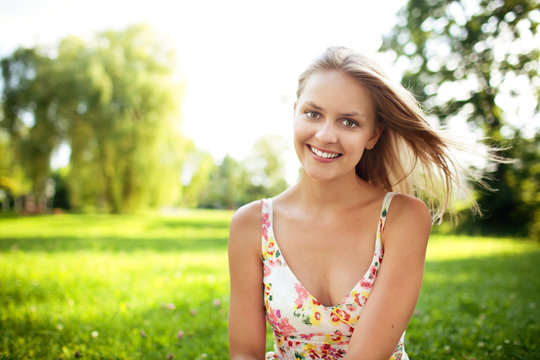 Beautiful young woman sitting on grass at park smiling
