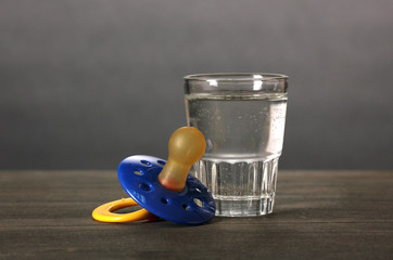 Baby dummy with alcoholic beverage on grey background
