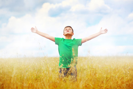 A boy standing in a field of wheat against cloudy sky background