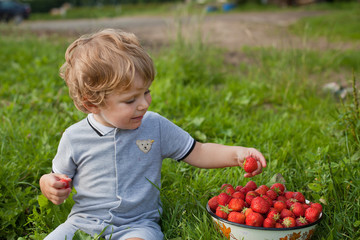 Sweet toddler with blond hairs on strawberry field