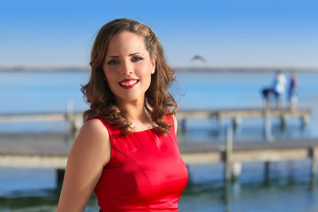 Fototapeta na wymiar Brunette kobieta w czerwonym sukienka uśmiecha zrelaksowany na jeziorze