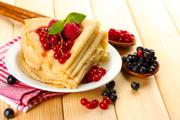Delicious pancakes with berries and jam on plate on wooden