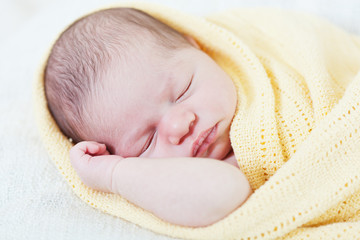 sleeping newborn baby wrapped in a yellow blanket