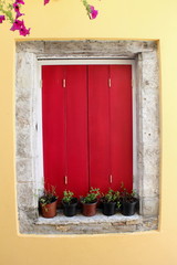 bright red wood painted closed window shutters framed with stone with plants and pots on the sill
