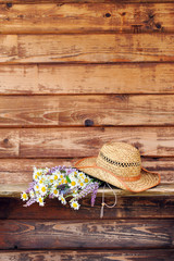 Wild flowers with straw hat on old boards  background