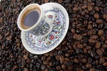 Cup of black coffee on a saucer on roasted coffee beans  