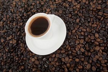 Cup of black coffee on a saucer on roasted coffee beans  