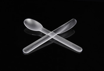 Plastic knife and spoon on black mirror background