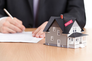 Businessman signs contract behind house architectural model