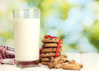 glass of milk, chocolate chips cookies with red ribbon and
