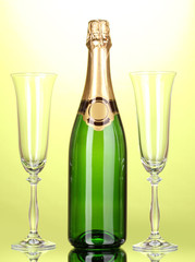 Bottle of champagne and goblets on green background